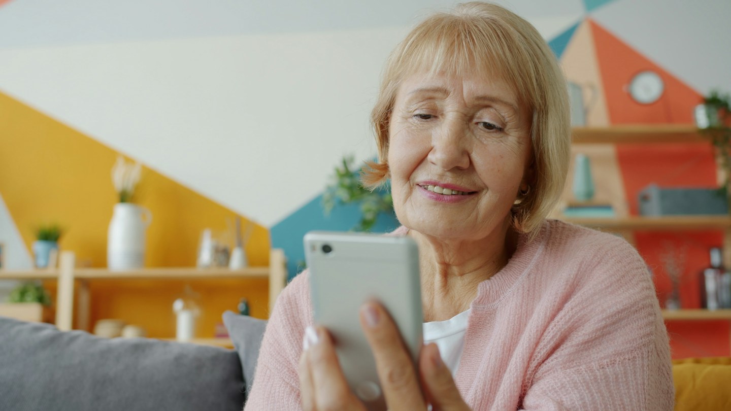 An older woman uses a smartphone at home.